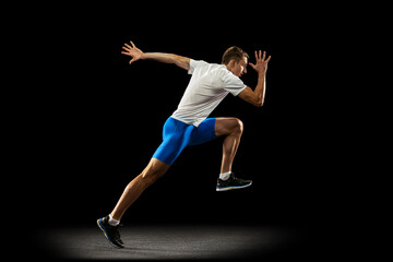 Portrait of muscular, sportive man, male athlete, runner training isolated on dark studio background with spotlight. Concept of action, motion, youth, healthy lifestyle.