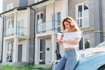 Waiting for the charge to finish. Young woman in casual clothes with her electromobile outdoors at daytime