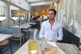 Fototapeta  - Przystojny, uśmiechnięty, dojrzały brunet z lampką wina podczas klimatycznej kolacji we włoskich klimatach. 