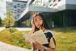 With book in hands. Young asian woman is outdoors at daytime