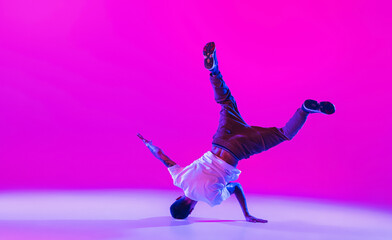Wall Mural - Young stylish man, hip-hop dancer dancing solo in modern clothes isolated over bright magenta background at dance hall in neon light.