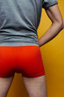 A sporty LGBT guy in tight colored boxers poses against a background of colored paper. body parts: elastic male buttocks. a man who is fond of fitness training