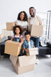 © LIGHTFIELD STUDIOS - happy african american family with carton boxes looking at camera in new apartment