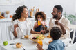 african american girl drinking orange juice during breakfast with family