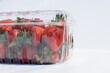 Clear plastic containers of fresh red, ripe strawberries with the stems still on them. The packages are stacked on top of each other on a grocery store shelf.  The berries are firm, rich, and vibrant.
