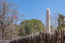 Jamestowne, VA, USA - April 1, 2013: Historic Site. Tencentennial Obelisk Monument Seen Over Defense Wall Of Fort Against Blue Sky. Some Green Foliage And British Flag.