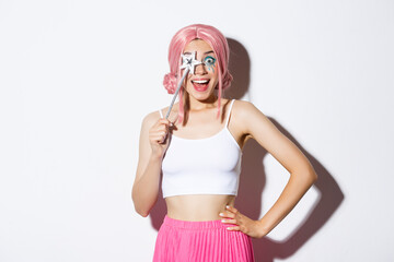 Portrait of happy girl smiling, celebrating halloween in fairy costume, with pink wig and bright makeup, holding magic wand, looking excited