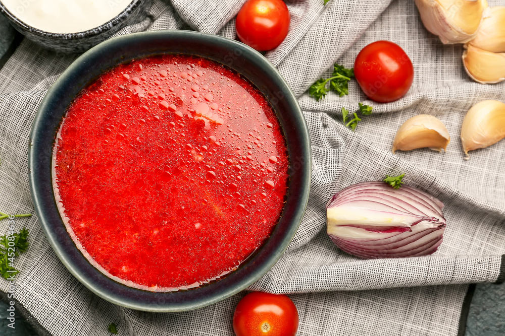 Bowl with tasty borscht and ingredients on table