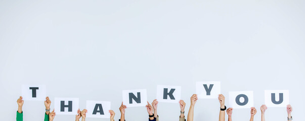 Studio shot of unrecognizable unidentified group of staff officer in corporate office holding thank you alphabet cardboard paper sign over head showing appreciation to customer on white background