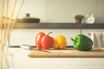 Sticker - Cutting board with red, yellow and green sweet bell peppers on a modern kitchen background. Vegetable ingredient, cooking healthy food concept