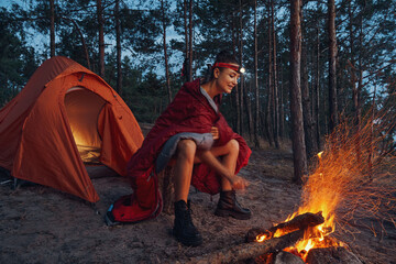 female warming up near campfire while wearing blanket on shoulders