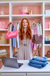 © alfa27 - Positive Woman Holding Two Different Handbags, Comparing Trends Fashion And Style. Cheerful Caucasian Stylist Lady Posing At Camera, Have Fun, Smile. Wardrobe With Many Outfits In The Background