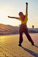 Wall Mural - sporty athletic woman with dyed pink hair stands back, stretches against background of sunset