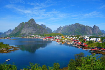 Reine in Lofoten Islands, Norway, with traditional red rorbu huts under blue sky with clouds.