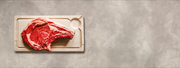 Wall Mural - Beef prime rib and wooden cutting board isolated on light concrete background. Horizontal banner