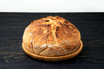 Fresh homemade wheat bread on wooden plate on black wooden table