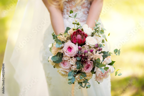 Bride in a dress standing in a green garden and holding a wedding bouquet of flowers and greenery. Wedding concept
