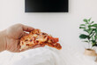 Person on bed and eating pizza watch television. Concept of stay home.
