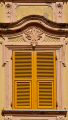 Sticker - Close-up of the closed window of an old palace with yellow shutters and bas-relief decoration, Italy