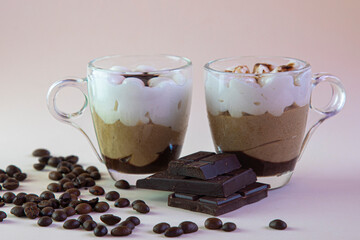 two transparent cups with cappuccino coffee, coffee grains and a bar of chocolate on a light background