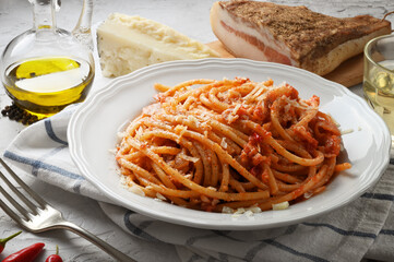 Amatriciana pasta. Bucatini amatriciana, with peeled tomatoes, pecorino cheese, bacon, extra virgin olive oil, white wine, pepper and chilli. Basic ingredients on white plaster background, close-up.