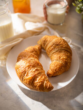 Two Mouth-watering Croissants On A White Earthenware Plate, In The Background Is A Glass Of Milk. White Silk Tablecloth. Close-up. High Angle View. Restaurant, Hotel, Cafe, Bakery.