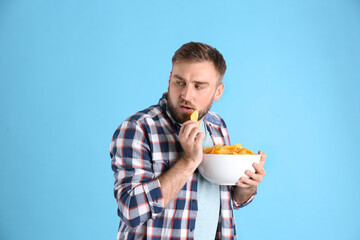 Wall Mural - Greedy young man hiding bowl with chips on light blue background