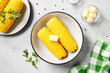 Cooked corn on the cob served with salt and butter. Light gray background. Top view