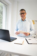 © epiximages - business man with blue shirt and black glasses is standing behind standing table and is working with his tablet and a black laptop in a modern office