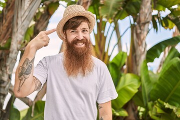 Canvas Print - Caucasian man with long beard outdoors on a sunny day wearing summer hat smiling happy pointing with hand and finger