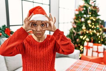 Poster - Young hispanic woman with short hair wearing christmas hat sitting on the sofa trying to open eyes with fingers, sleepy and tired for morning fatigue