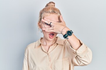 Poster - Beautiful caucasian woman with blond hair wearing casual look and glasses peeking in shock covering face and eyes with hand, looking through fingers with embarrassed expression.