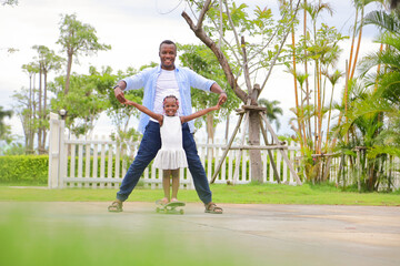 Wall Mural - African American father teach his little daughter to play skateboard in the public park during summer time