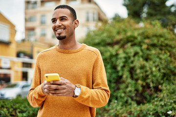 Wall Mural - Young african american man smiling happy using smartphone at the city.