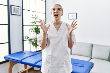 Poster - Young caucasian physiotherapy woman working at home crazy and mad shouting and yelling with aggressive expression and arms raised. frustration concept.