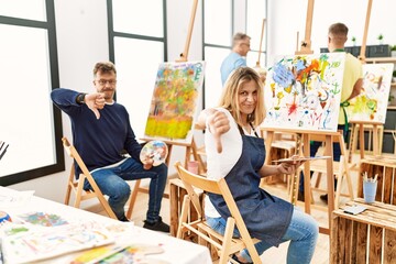 Sticker - Group of middle age artist at art studio looking unhappy and angry showing rejection and negative with thumbs down gesture. bad expression.