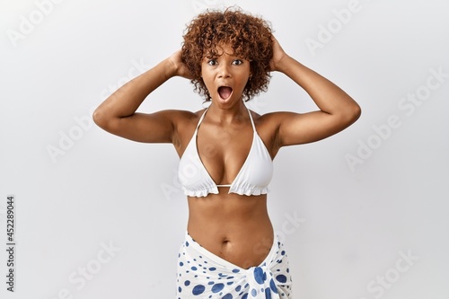 Young african american woman with curly hair wearing bikini crazy and scared with hands on head, afraid and surprised of shock with open mouth