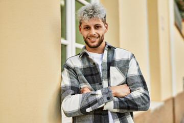 Wall Mural - Young hispanic man smiling happy with arms crossed gesture at the city.