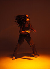 Wall Mural - Dancing mixed race girl inshadow in studio. Female dancer performer moving in expressive ethnic hip hop dance