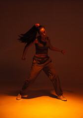 Wall Mural - Dancing athletic mixed race girl performing expressive fiery hip hop or ethnic afro dance in warm studio light