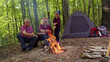 © Andrii Iemelianenko - Senior elderly grandmother grandfather with granddaughter cooking frying sausages over campfire in wood. Old man woman and child girl kid tourists having camping in forest. Active rest of family