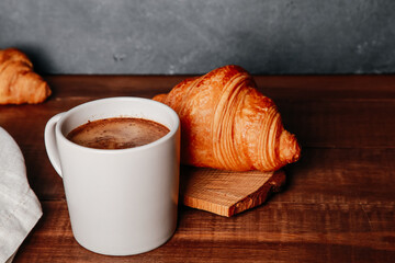 Fresh baked croissants, mug of black coffee on brown wooden table. Cup of hot Americano with foam, buns, rolls close up. Food, French breakfast, morning menu, cafe concept. Side view