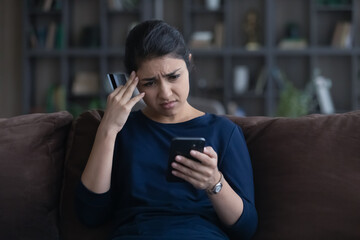 Unhappy young Indian woman distressed with payment problems shopping online from home on smartphone with credit debit card. Upset biracial female buyer frustrated with bank error on cell.