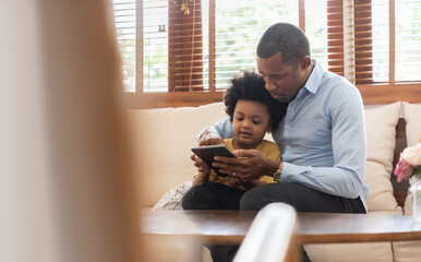 Wall Mural - Happy Black African American Brazilian father and little boy using digital tablet