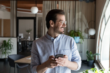 Wall Mural - smiling young caucasian male employee look in distance use modern smartphone gadget text message onl