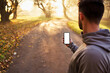 © baranq - Runner looking on smartphone with empty, blank screen during sunny autumn morning