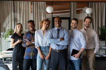 Wall Mural - Portrait of smiling multiracial team pose together in modern office show unity and leadership. Happy African American male boss or businessman with multiethnic employees. Diversity, business concept.