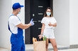 © romaset - Young courier wearing a protective mask and gloves delivers goods to a young woman during quarantine
