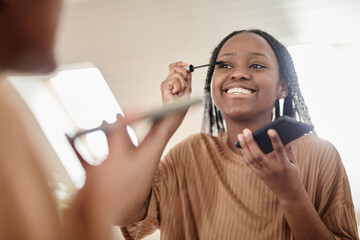 Wall Mural - Portrait of young African-American woman putting on mascara while doing makeup in morning and smiling at camera