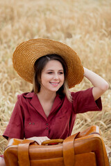 Sticker - young woman with vintage suitcase and hat on a yellow wheat field